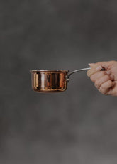 Vogue copper mini saucepan held by hand on seamless grey backdrop